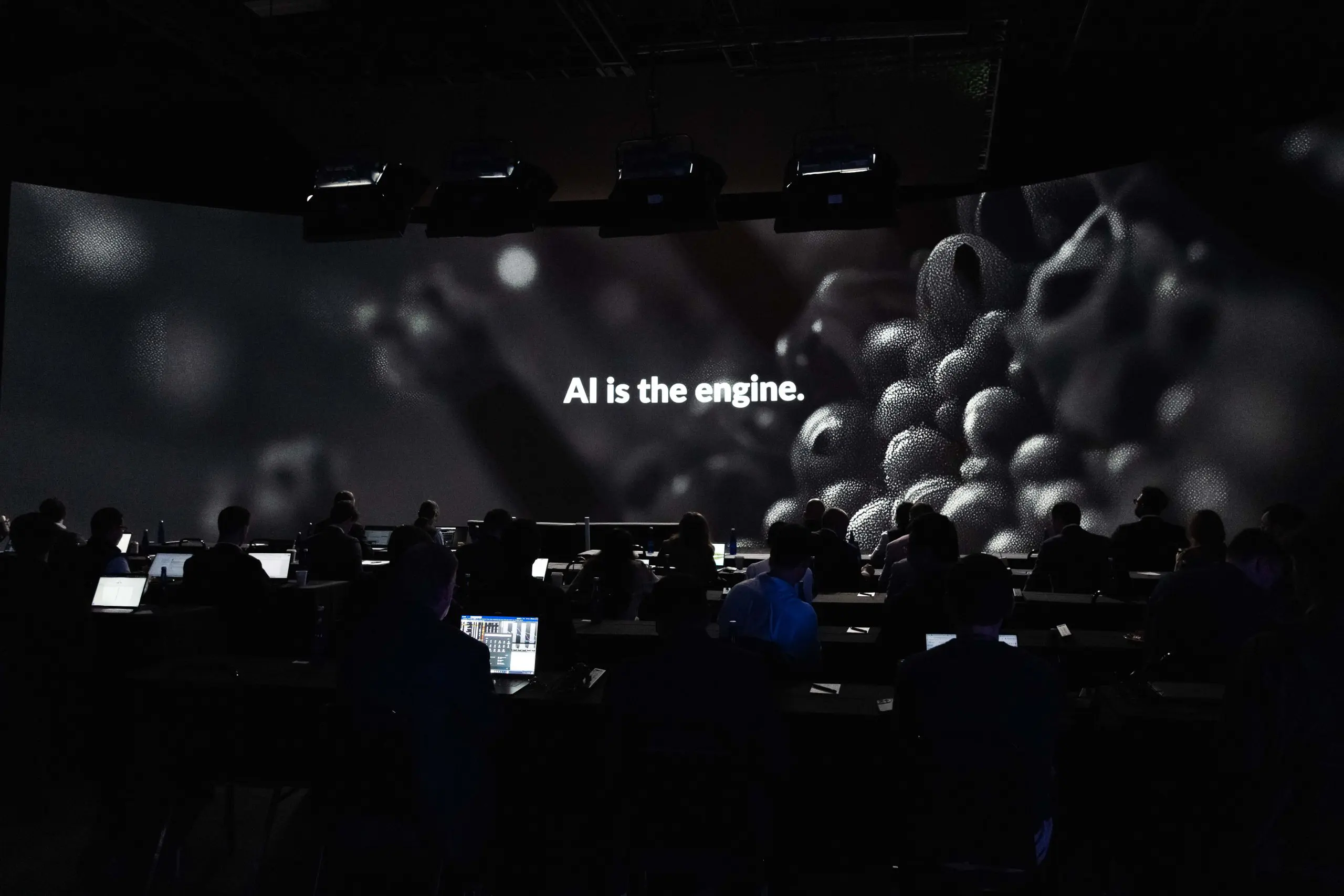 Audience engaged in a presentation with a large screen displaying the text "AI is the engine," highlighting the importance of artificial intelligence in technology and innovation.