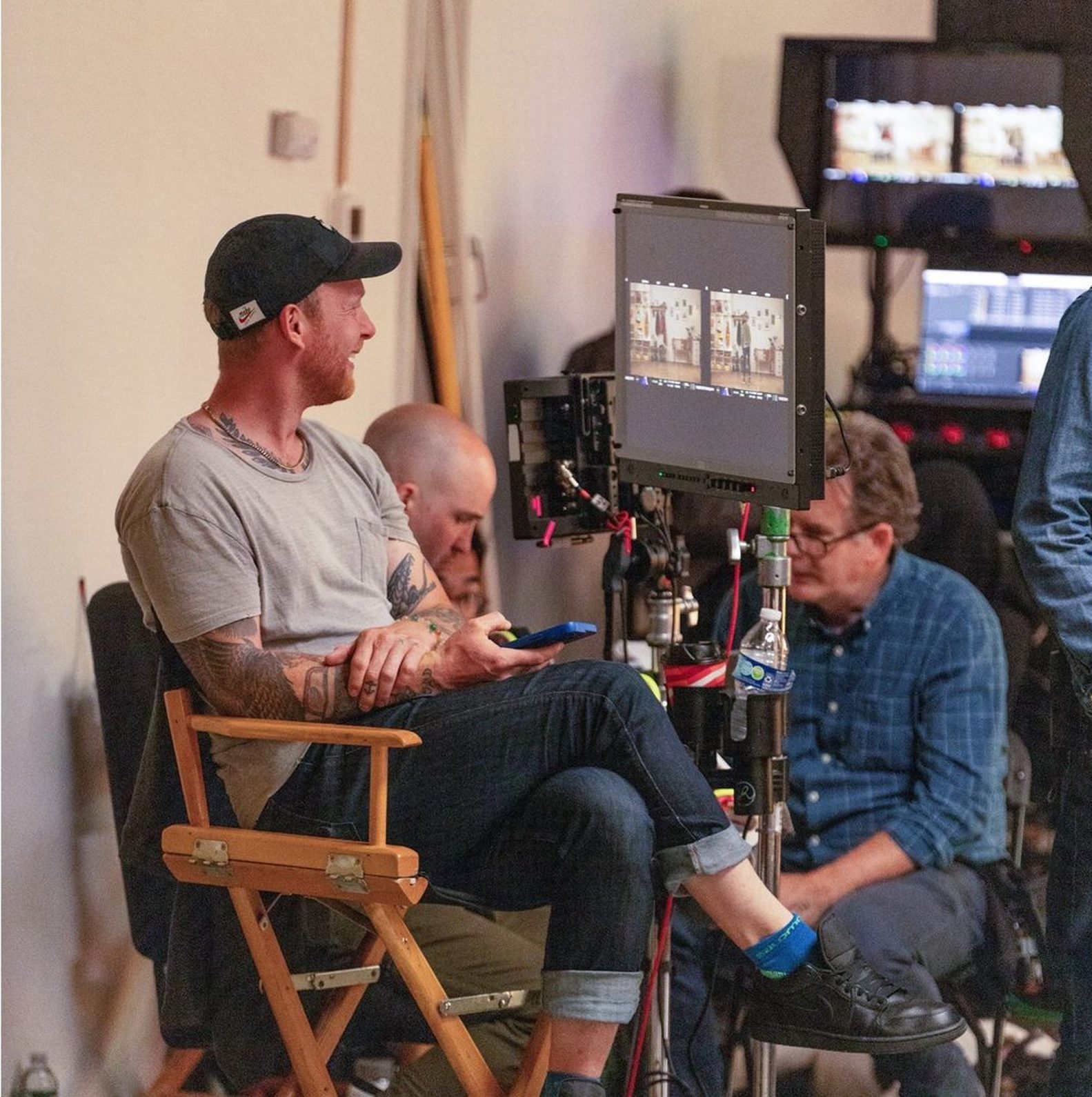 Behind-the-scenes image of a film set, featuring a director sitting on a chair, reviewing footage on a monitor. The scene captures crew members working in the background, showcasing the collaborative environment of film production.