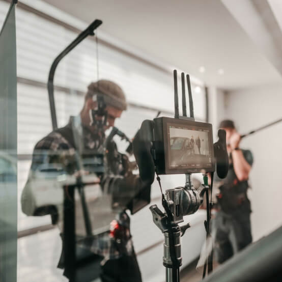 Filmmakers setting up equipment in a modern studio, featuring a camera monitor displaying a scene, with crew members preparing for a video shoot.