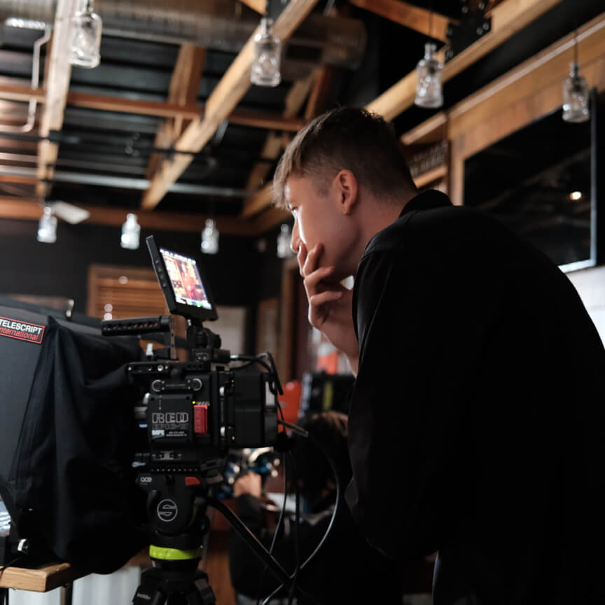Young male filmmaker focused on a camera monitor during a video production in a modern studio setting.