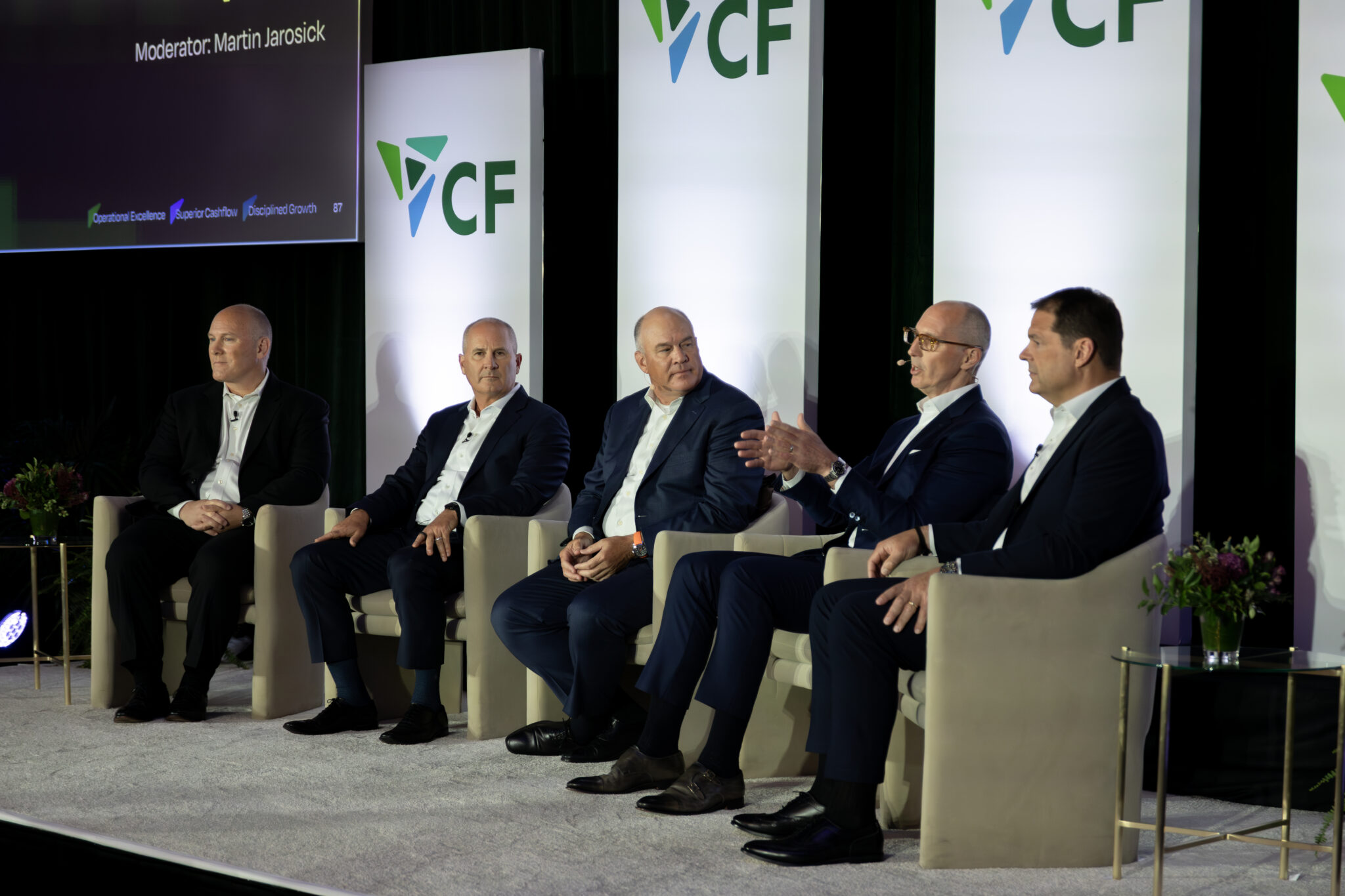 Panel discussion featuring five speakers at a business conference, moderated by Martin Jarosick. The backdrop displays the CF logo, and the speakers are engaged in conversation about industry trends and insights.