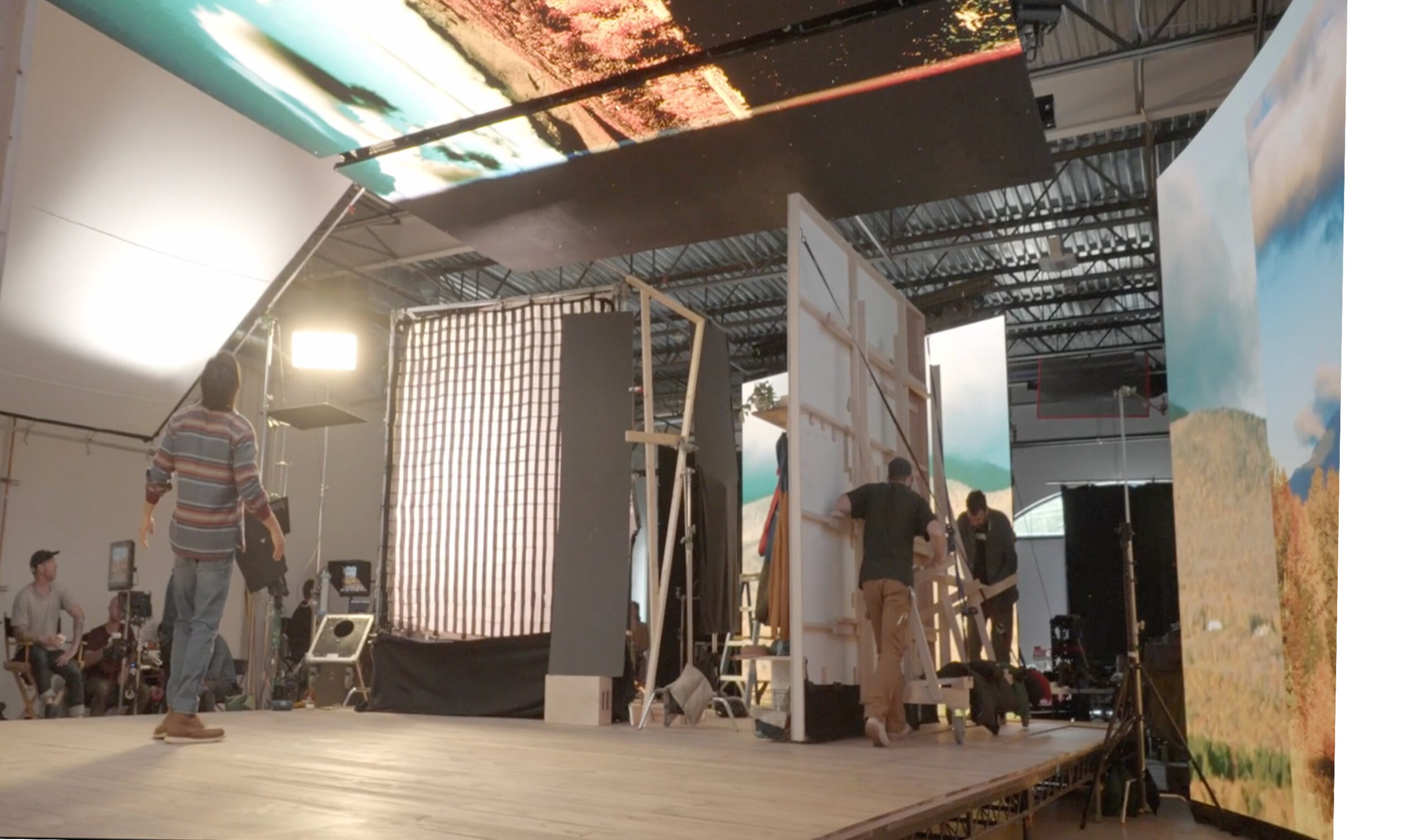 Behind-the-scenes view of a film set with crew members adjusting large backdrop panels and lighting equipment, showcasing a staged environment for a production.