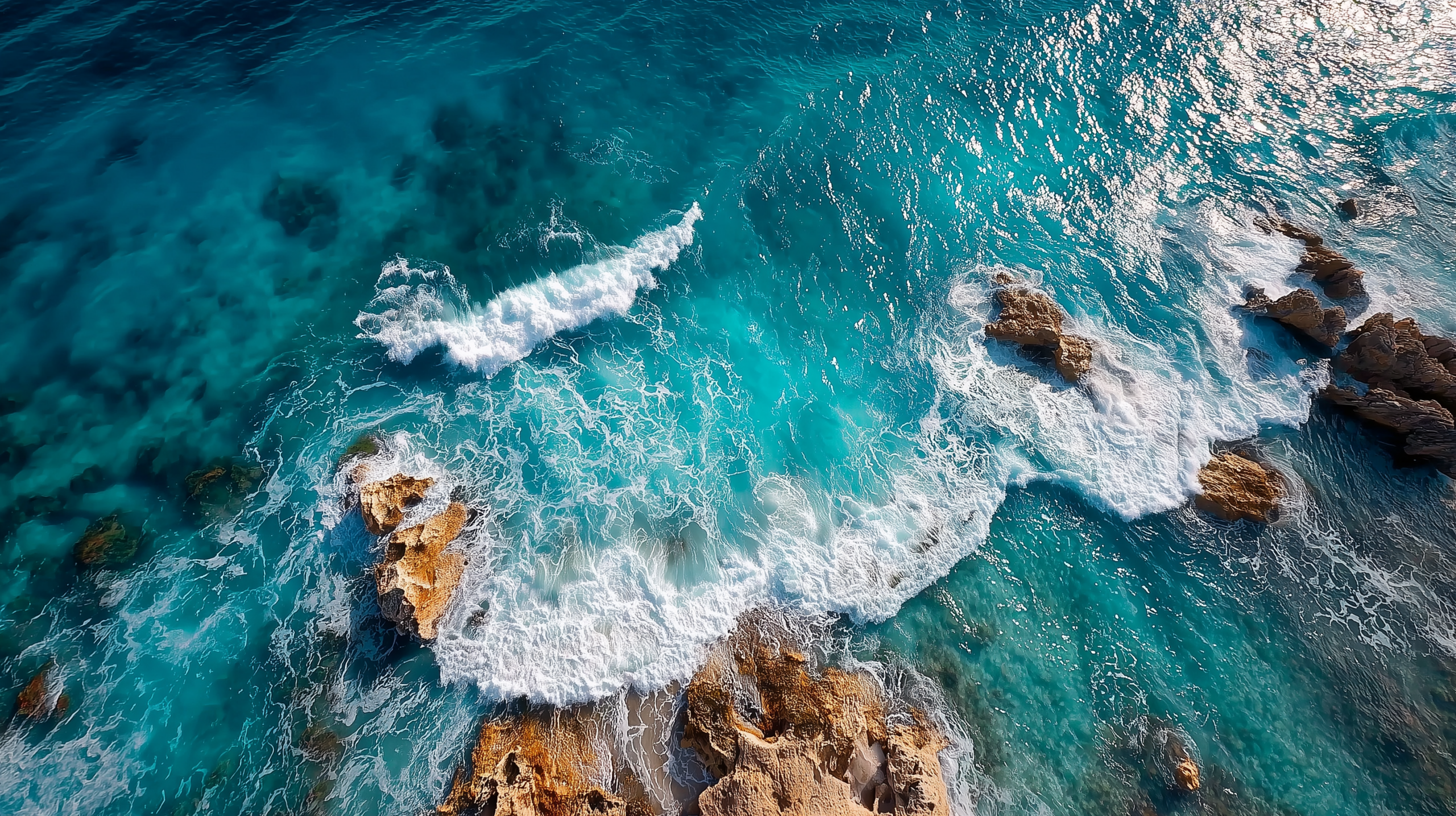 Aerial view of turquoise ocean waves crashing against rocky coastline, showcasing the vibrant colors of the water and the texture of the rocks.