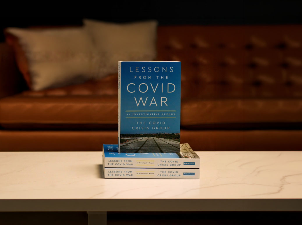 Book titled "Lessons from the COVID War" by The COVID Crisis Group, displayed on a table with a leather couch in the background. The book provides insights and analysis on the COVID-19 pandemic.
