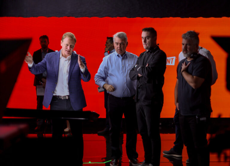 Group of professionals discussing a project on set, with a vibrant red background. The scene captures a collaborative atmosphere among team members, showcasing creative brainstorming and leadership in a production environment.