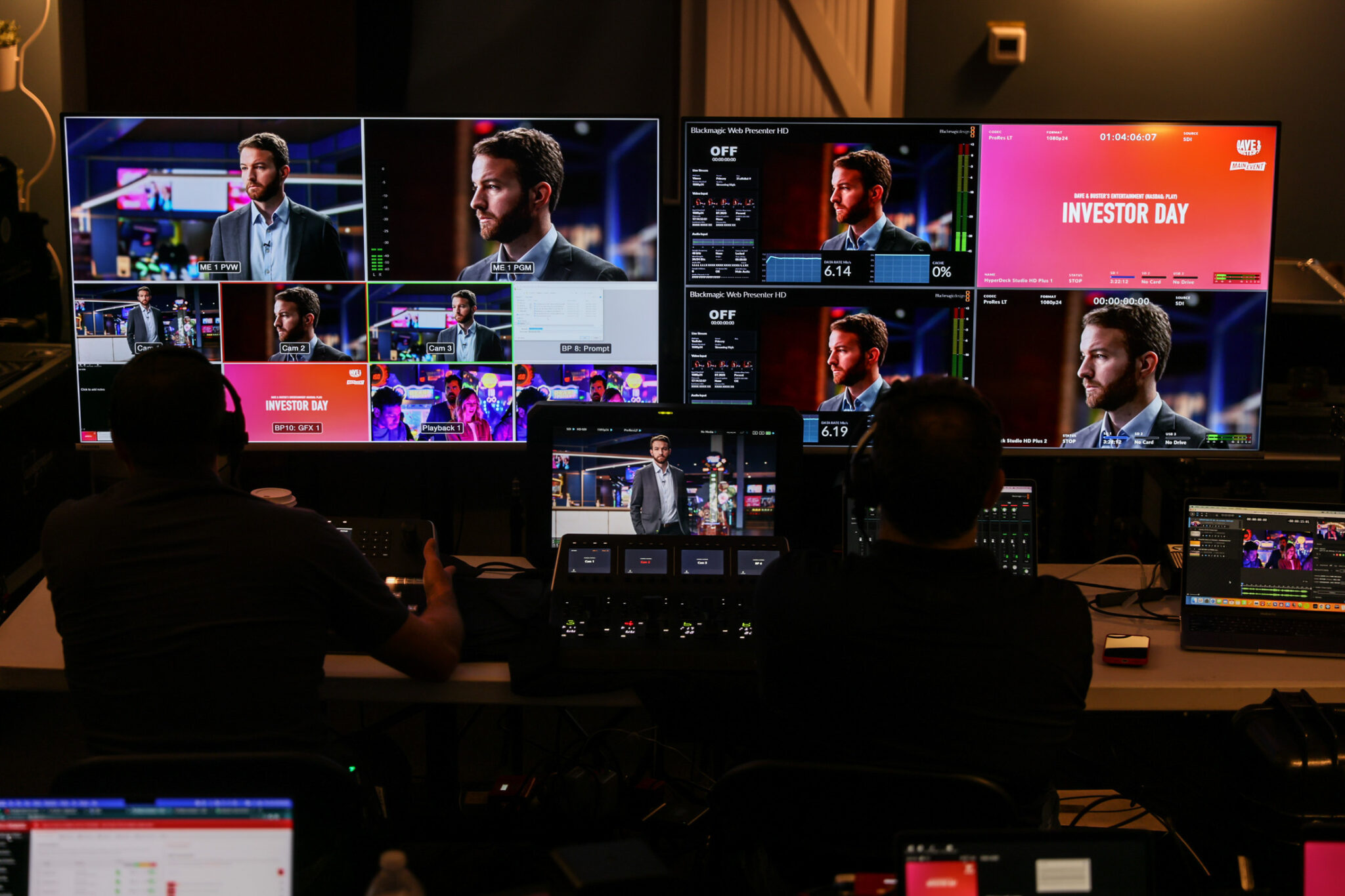 Control room setup for a live event featuring multiple screens displaying a speaker during an Investor Day presentation, with operators managing video feeds and graphics.