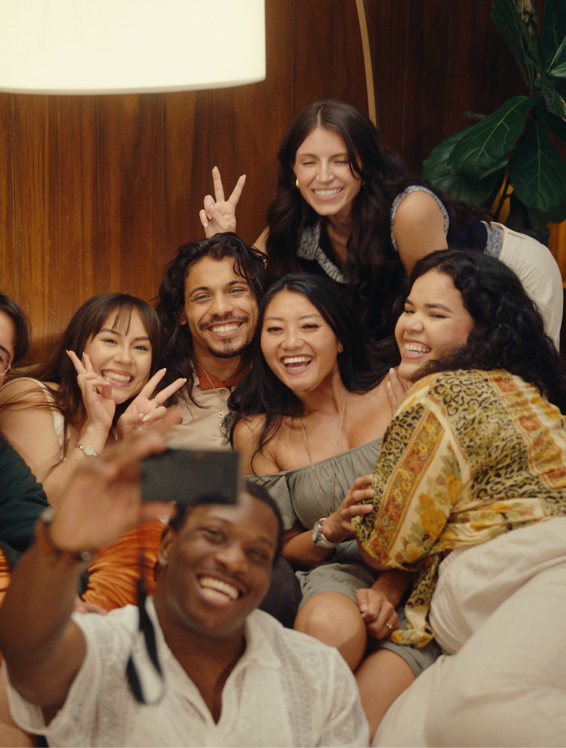 Group of friends smiling and posing for a selfie in a cozy living room setting, featuring a mix of diverse individuals enjoying a fun gathering.