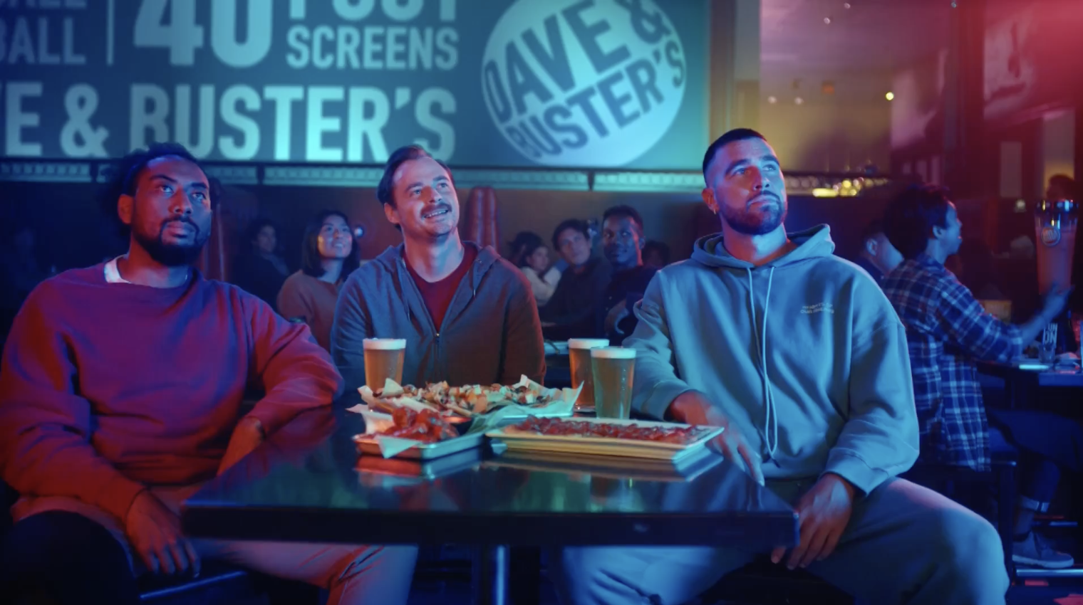 Group of friends enjoying food and drinks while watching a game at Dave & Buster's. The vibrant atmosphere features large screens and a lively crowd, highlighting the excitement of the sports viewing experience.