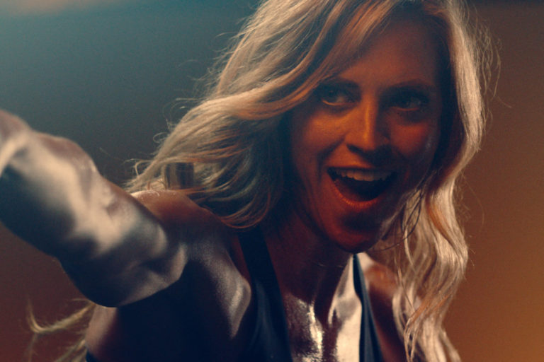 Motivated female athlete with long hair, smiling and engaging in an intense workout, showcasing strength and determination in a dynamic fitness environment.