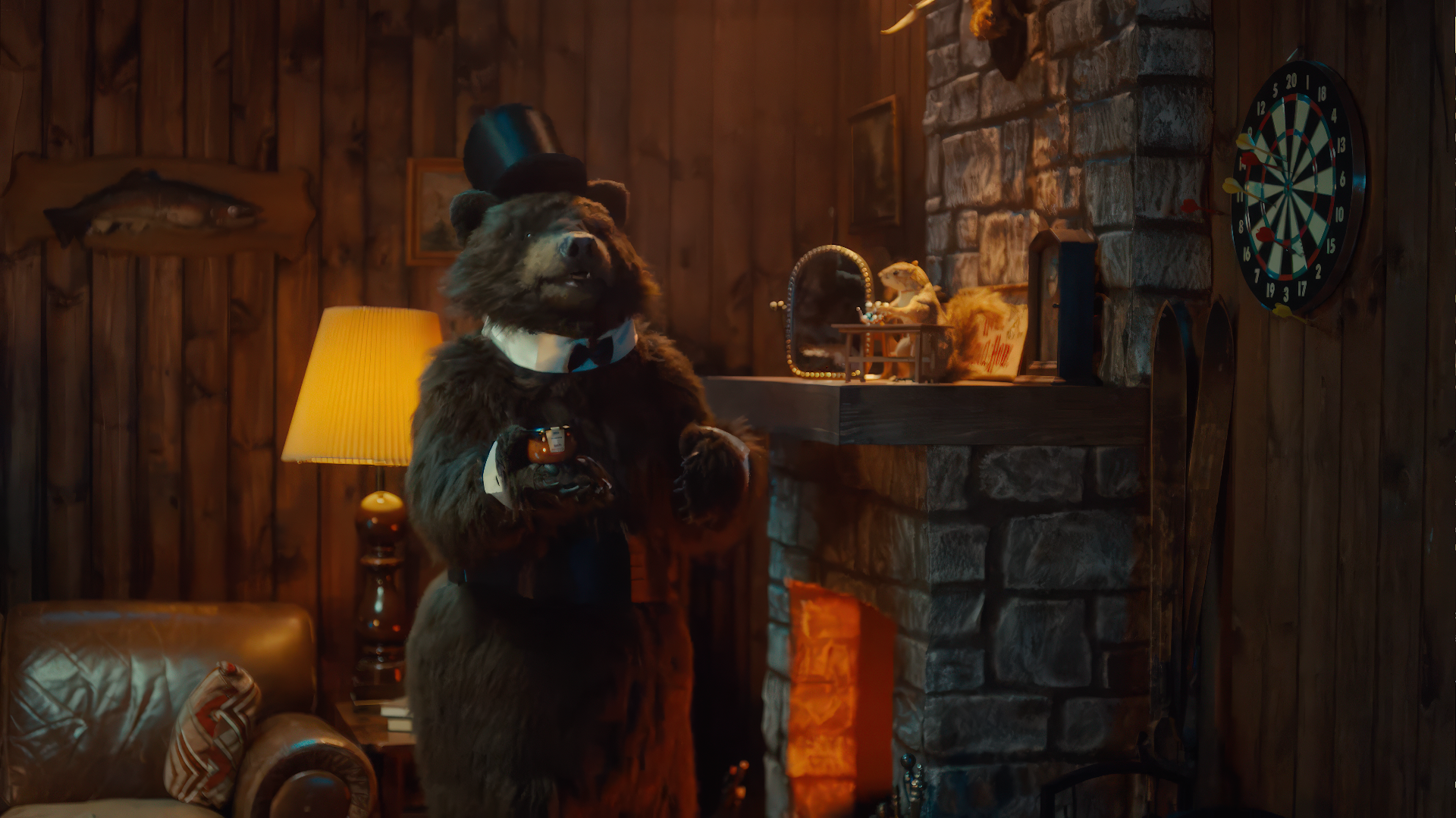 A bear in a formal outfit, complete with a top hat and bow tie, stands in a cozy, rustic room with a stone fireplace, wooden walls, and a dartboard. The bear holds a drink, adding a whimsical touch to the warm, inviting atmosphere.