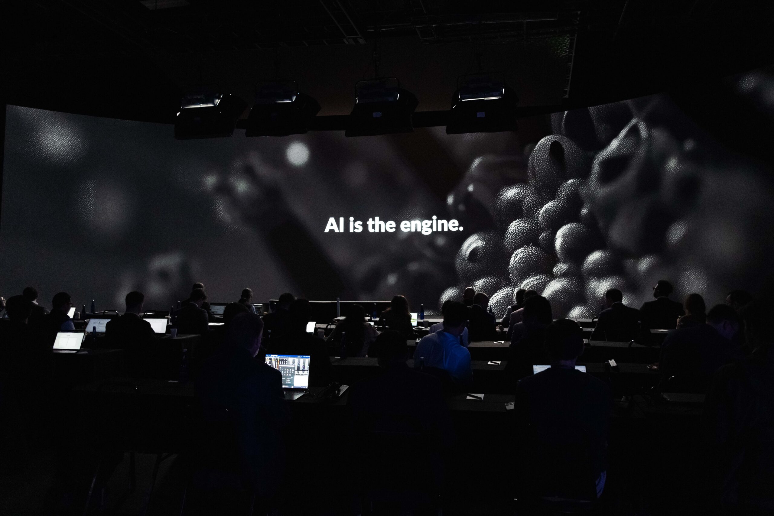 Audience engaged in a presentation with a large screen displaying the text "AI is the engine," highlighting the importance of artificial intelligence in technology and innovation.